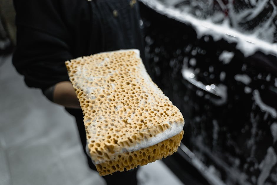 A person cleaning the exterior of a car with a sponge and water.